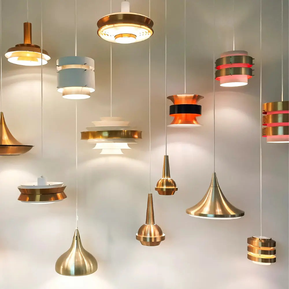 Kolekce 12 závěsných stropních svítidel v bronzových, zlatých a bílých odstínech, visících na bílých kabelech proti šedé stěně – moderní minimalistický design se slevou až 68 %