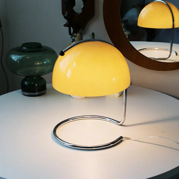 Designová stolní lampa Boun ve oranzova barvě na bílém stole – moderní svítidlo se skleněným stínidlem a chromovanou konstrukcí.