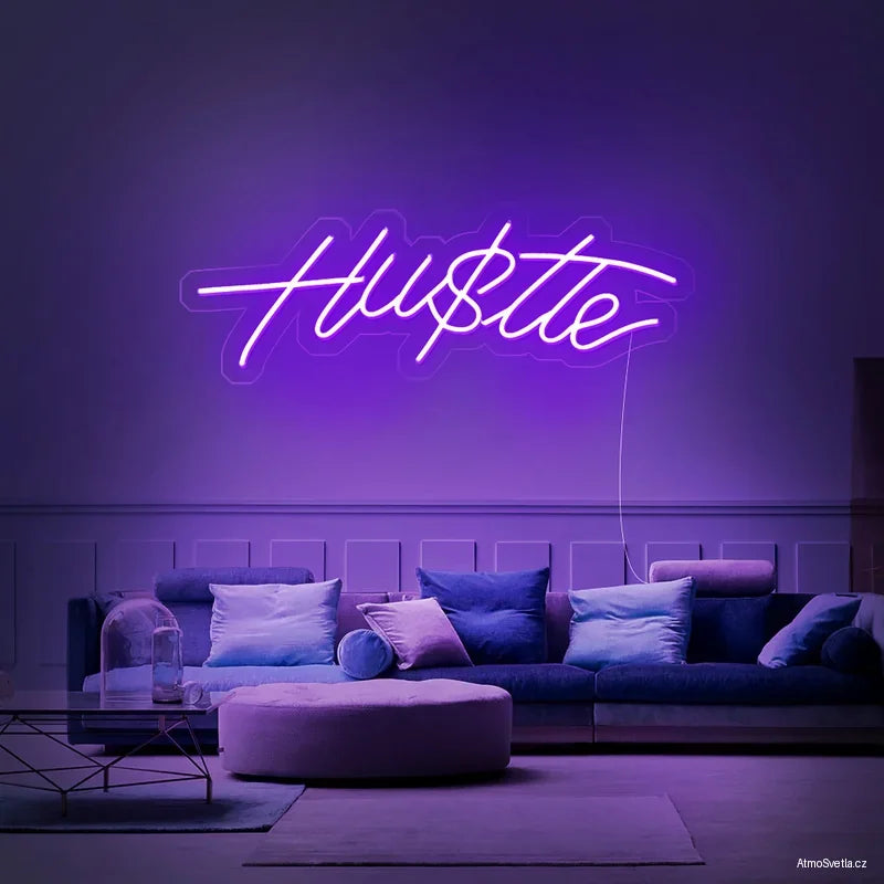 Fialově svítící nápis Hustle, moderní LED neonová dekorace nad sedací soupravu.