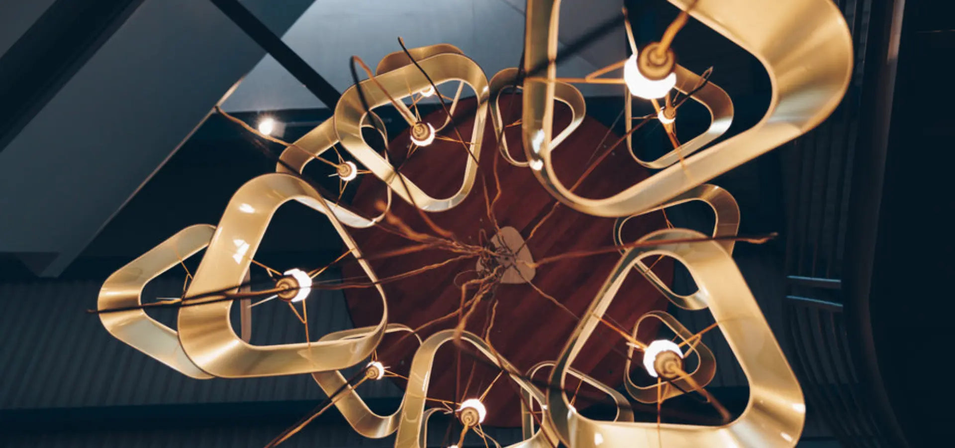 Moderní závěsný lustr s geometrickými prvky a teplým světlem, pohled zespodu.