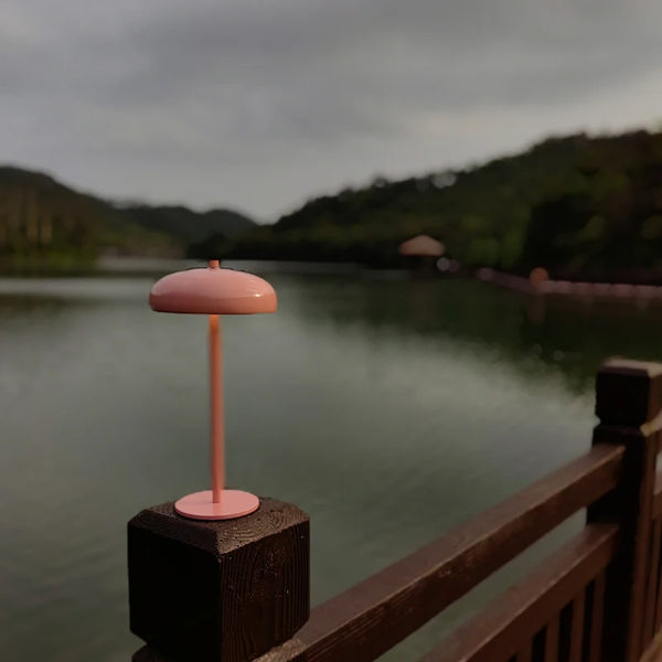 Stolní lampa Mushroom v růžové barvě na dřevěném zábradlí u jezera – stylové dobíjecí LED svítidlo v přírodě.