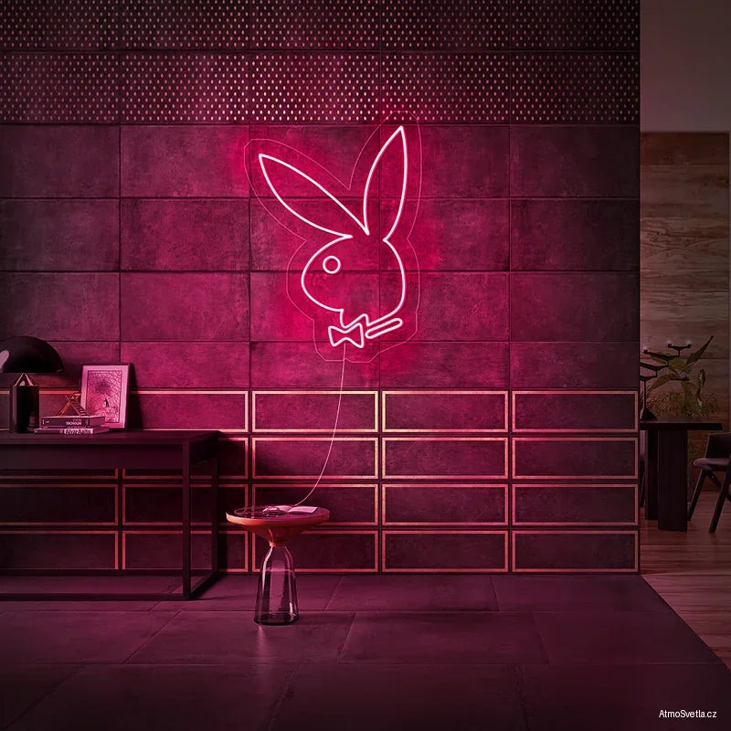 Růžový neonový nápis Playboy zajíček na tmavé stěně v moderním interiéru.