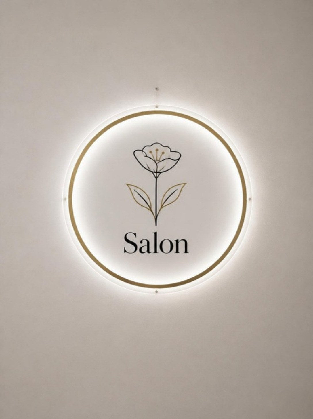 Podsvícené kruhové logo salonu se zlatým rámem na zdi