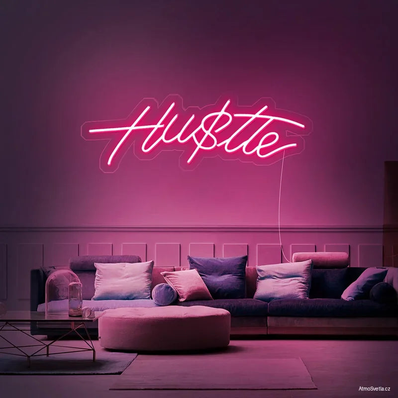 Růžový neonový nápis Hustle nad pohovkou, moderní světelná dekorace do interiéru.